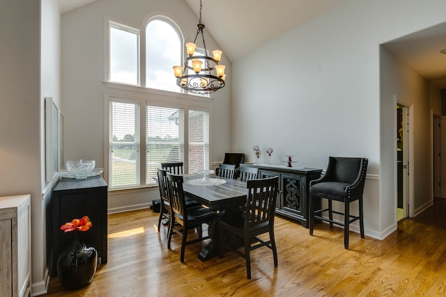 dining space featuring light hardwood / wood-style floors, high vaulted ceiling, and an inviting chandelier