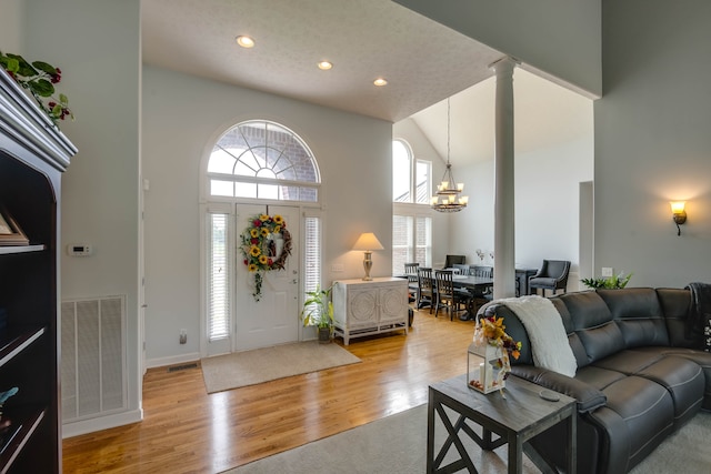 foyer featuring high vaulted ceiling, light hardwood / wood-style floors, ornate columns, and a chandelier