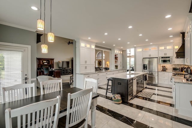 kitchen featuring custom range hood, appliances with stainless steel finishes, white cabinetry, tasteful backsplash, and an island with sink