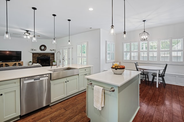 kitchen with stainless steel dishwasher, dark hardwood / wood-style floors, a stone fireplace, decorative light fixtures, and a center island with sink