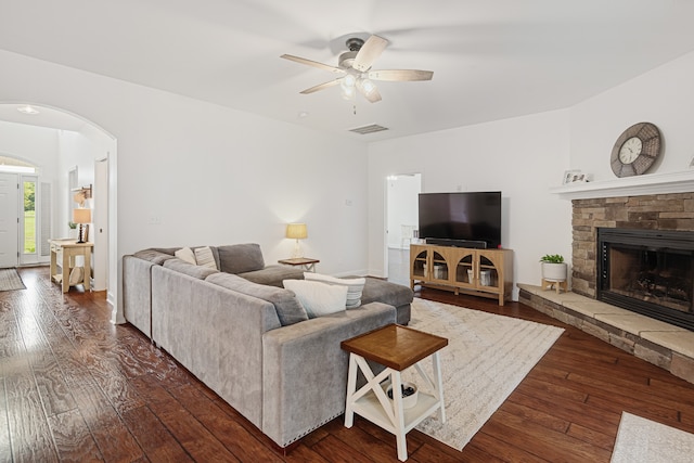 living room with ceiling fan, dark wood-type flooring, and a stone fireplace