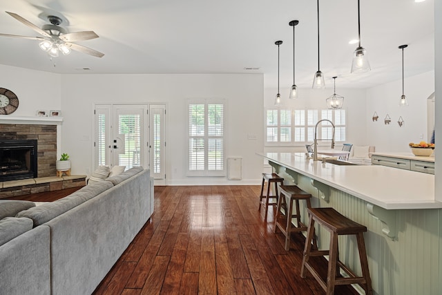 living room featuring ceiling fan, a stone fireplace, and dark hardwood / wood-style flooring