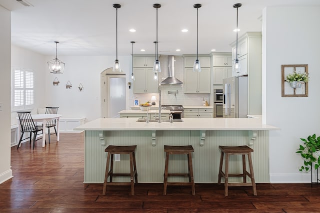 kitchen featuring a breakfast bar, dark wood-type flooring, wall chimney range hood, and hanging light fixtures