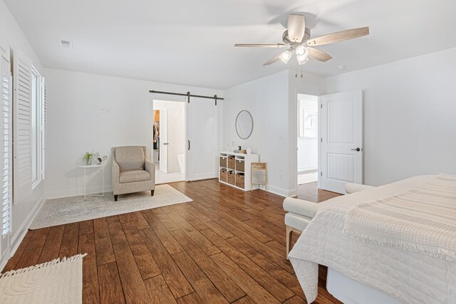 bedroom with ceiling fan, a barn door, and wood-type flooring