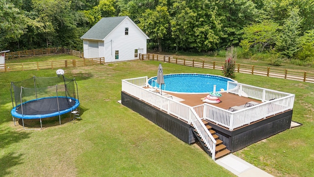 view of swimming pool with a trampoline, a wooden deck, and a lawn