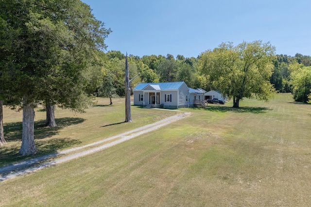 view of front of home with driveway, metal roof, a forest view, and a front lawn