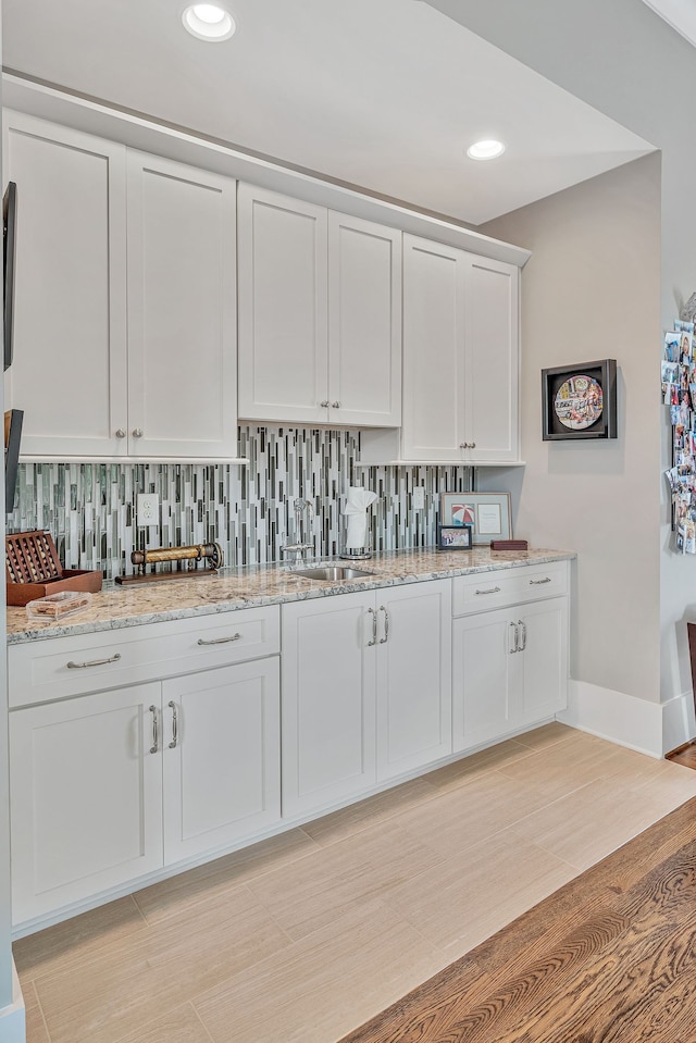 kitchen with light hardwood / wood-style flooring, light stone counters, decorative backsplash, and white cabinets