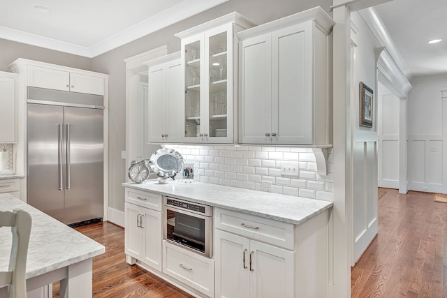 kitchen with dark hardwood / wood-style floors, light stone countertops, appliances with stainless steel finishes, crown molding, and white cabinets