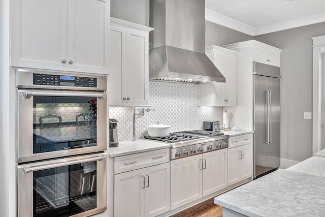 kitchen featuring ornamental molding, appliances with stainless steel finishes, white cabinets, and wall chimney exhaust hood