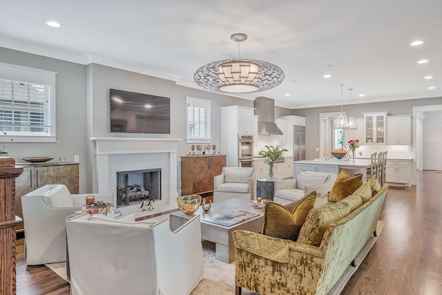 living room with crown molding, light hardwood / wood-style flooring, a tiled fireplace, and an inviting chandelier