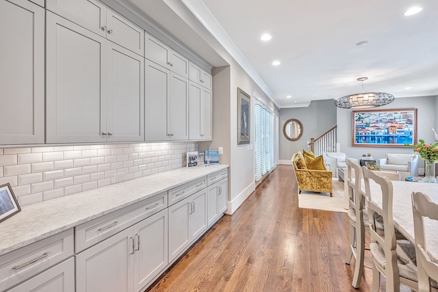 kitchen featuring pendant lighting, tasteful backsplash, light hardwood / wood-style floors, ornamental molding, and light stone counters