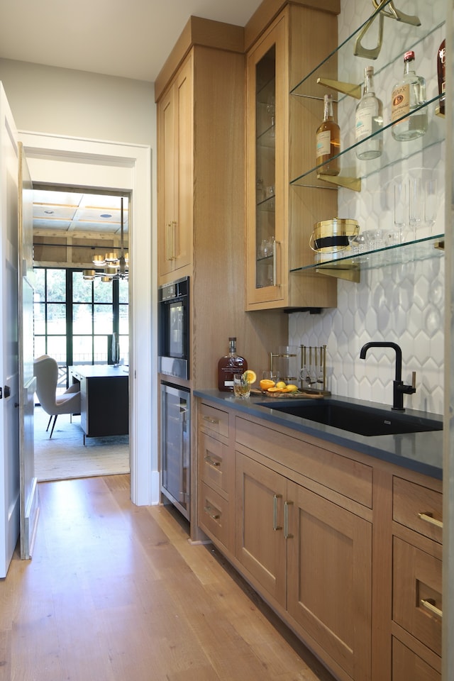 kitchen featuring light hardwood / wood-style flooring, oven, tasteful backsplash, beverage cooler, and sink