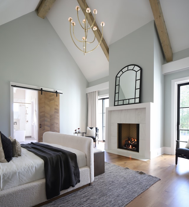 bedroom with a barn door, high vaulted ceiling, hardwood / wood-style flooring, and a tile fireplace