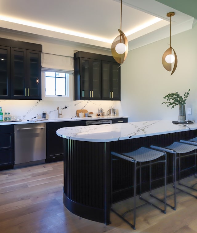 kitchen with dishwasher, light stone countertops, light hardwood / wood-style floors, a tray ceiling, and hanging light fixtures