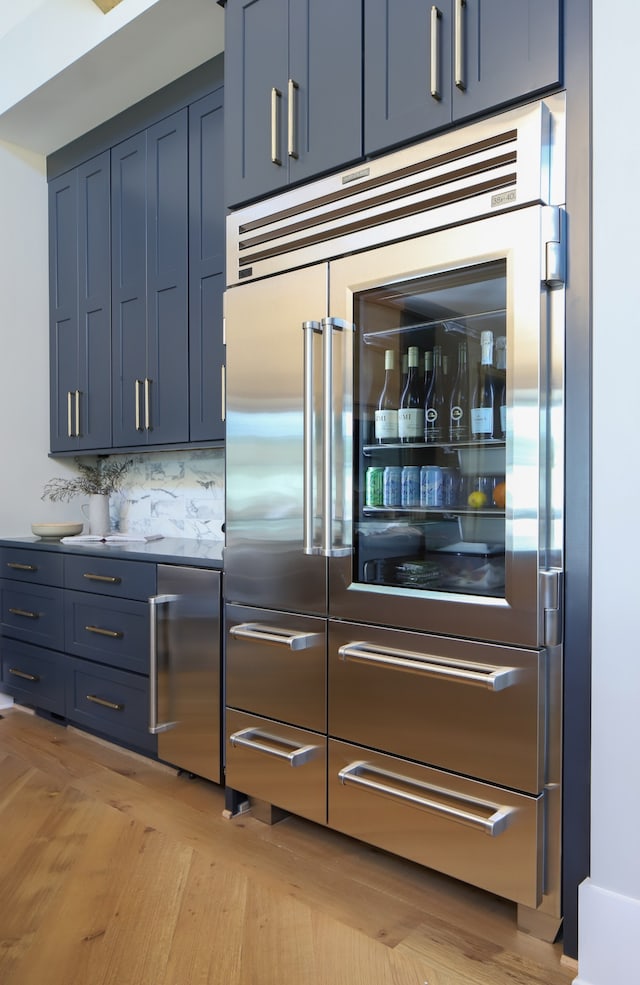 kitchen featuring light hardwood / wood-style flooring, blue cabinetry, decorative backsplash, and stainless steel built in fridge