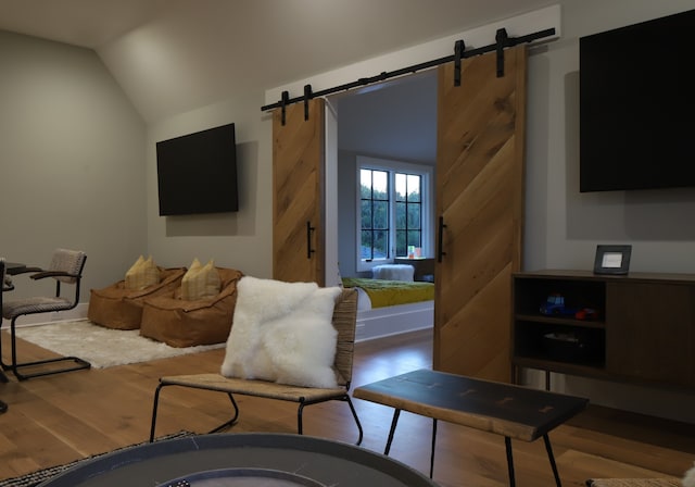 living room with light wood-type flooring, vaulted ceiling, and a barn door