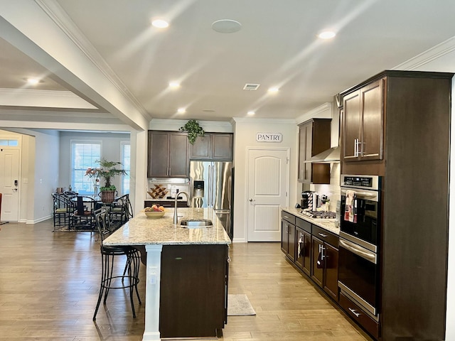 kitchen with dark brown cabinetry, appliances with stainless steel finishes, and a center island with sink