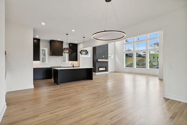 kitchen featuring light wood-type flooring, sink, hanging light fixtures, and an island with sink