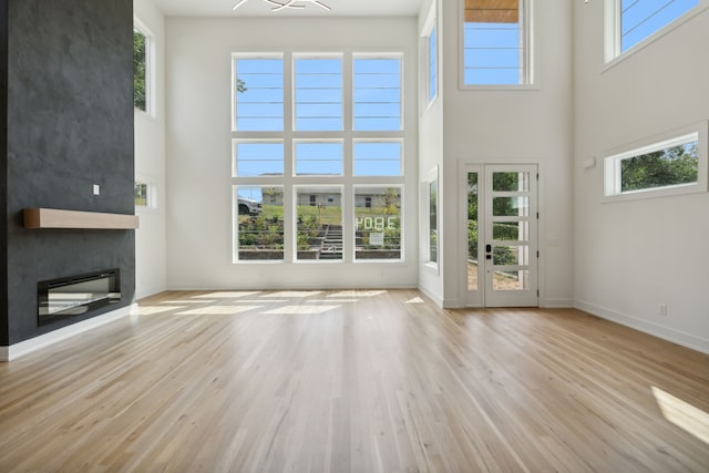 unfurnished living room with light hardwood / wood-style floors, a high ceiling, and plenty of natural light