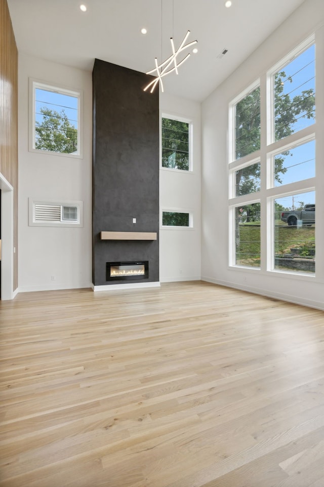 unfurnished living room with a fireplace, light wood-type flooring, a notable chandelier, and a towering ceiling