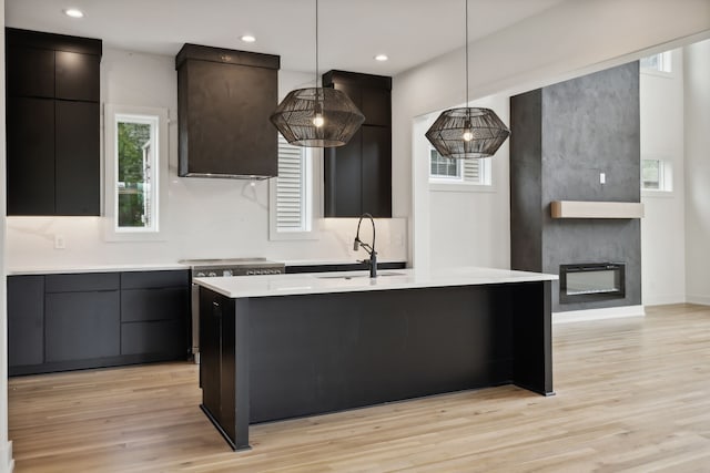 kitchen featuring decorative light fixtures, light hardwood / wood-style floors, sink, an island with sink, and a fireplace