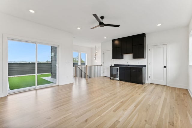 unfurnished living room with ceiling fan, sink, light hardwood / wood-style floors, and wine cooler