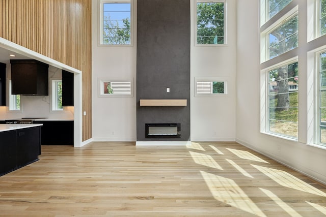 unfurnished living room with a towering ceiling, a fireplace, and light wood-type flooring