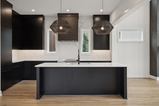 kitchen with light wood-type flooring, sink, decorative backsplash, and a center island with sink