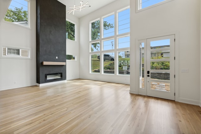 unfurnished living room with a towering ceiling, light hardwood / wood-style flooring, a large fireplace, and a chandelier