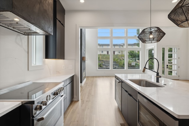 kitchen featuring light hardwood / wood-style floors, sink, light stone countertops, high end stove, and hanging light fixtures