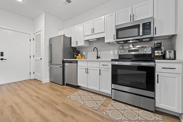 kitchen with appliances with stainless steel finishes, white cabinetry, sink, and light hardwood / wood-style flooring