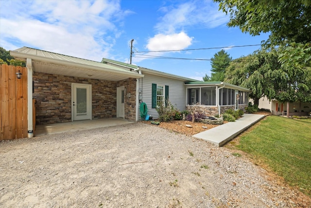 exterior space featuring dirt driveway, a front yard, a sunroom, a carport, and stone siding