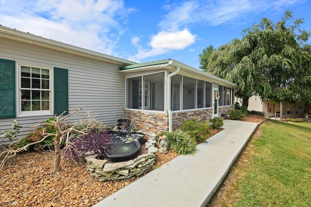 view of property exterior featuring stone siding, a yard, and a sunroom