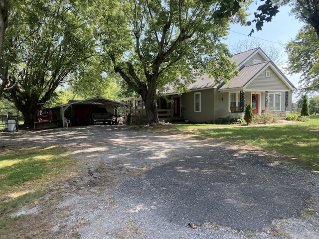 view of front of home featuring a detached carport, metal roof, gravel driveway, covered porch, and a front yard