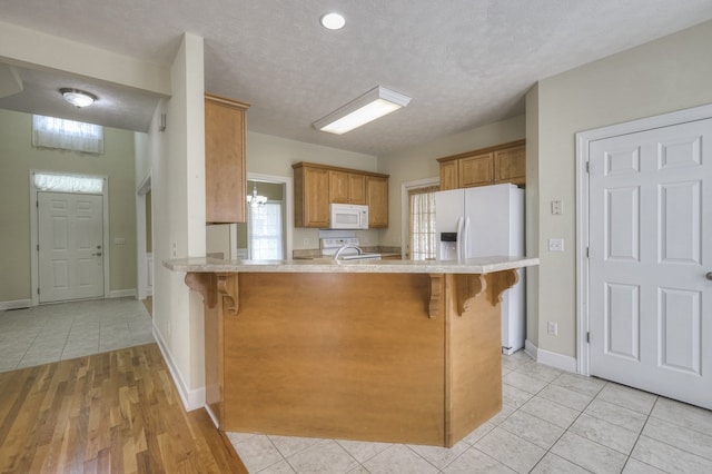 kitchen featuring kitchen peninsula, a kitchen breakfast bar, light hardwood / wood-style flooring, and white appliances