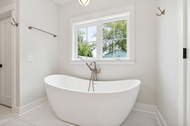 bathroom with a soaking tub, baseboards, and marble finish floor