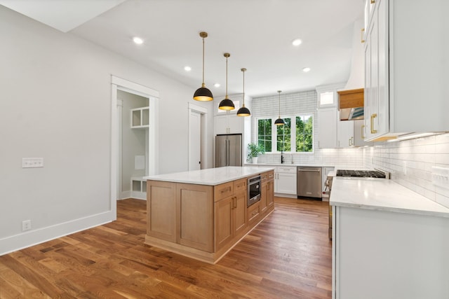 kitchen featuring light stone counters, white cabinetry, appliances with stainless steel finishes, a center island, and pendant lighting