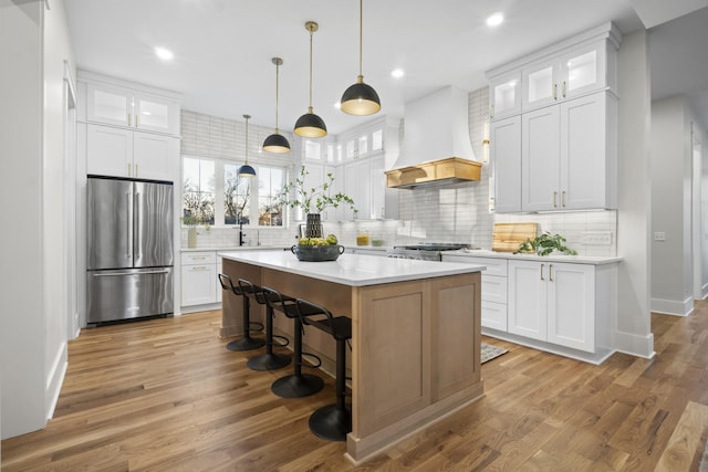 kitchen featuring glass insert cabinets, freestanding refrigerator, white cabinets, and custom range hood