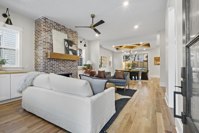 living area featuring a fireplace, light wood finished floors, recessed lighting, baseboards, and ceiling fan with notable chandelier