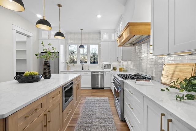 kitchen featuring white cabinets, stainless steel appliances, decorative light fixtures, and light stone countertops