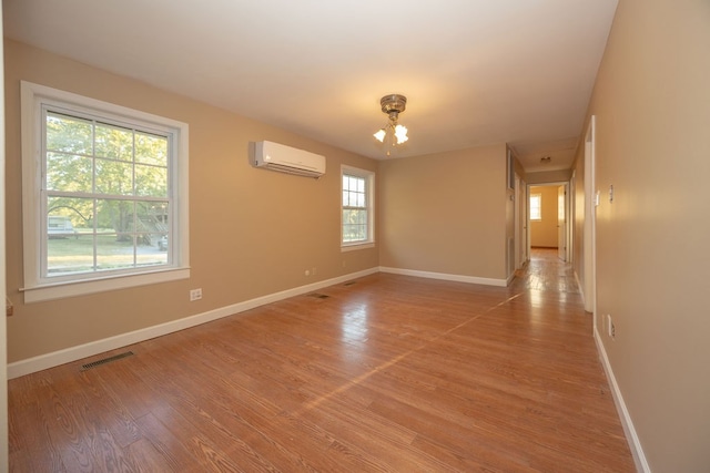 unfurnished room featuring a wall mounted air conditioner, light wood-type flooring, and a wealth of natural light