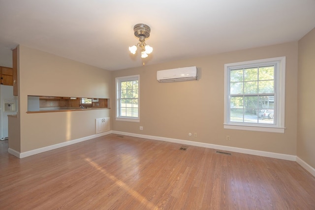 empty room featuring an inviting chandelier, light hardwood / wood-style flooring, and a wall unit AC