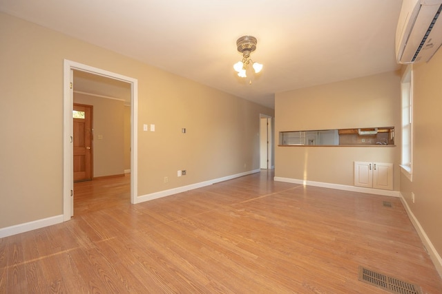 spare room featuring a wall mounted air conditioner, light wood-type flooring, and a notable chandelier