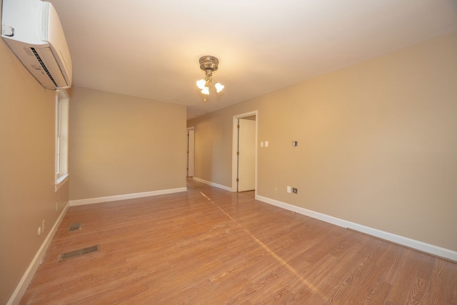 unfurnished room featuring light wood-type flooring, an AC wall unit, and an inviting chandelier