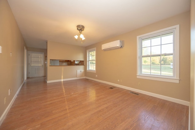 unfurnished living room with a notable chandelier, light hardwood / wood-style floors, a healthy amount of sunlight, and a wall unit AC