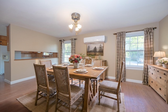 dining space featuring an inviting chandelier, an AC wall unit, a wealth of natural light, and light hardwood / wood-style flooring