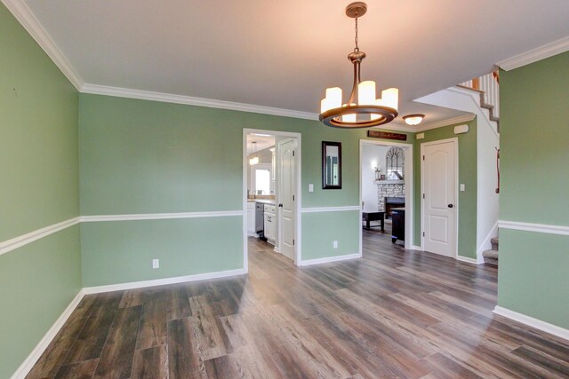 unfurnished dining area featuring a fireplace, crown molding, hardwood / wood-style floors, and a chandelier