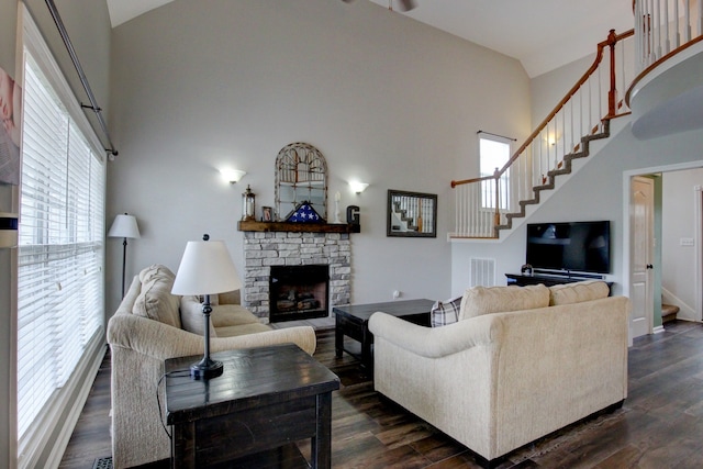 living room with a high ceiling, a healthy amount of sunlight, a stone fireplace, and dark hardwood / wood-style floors