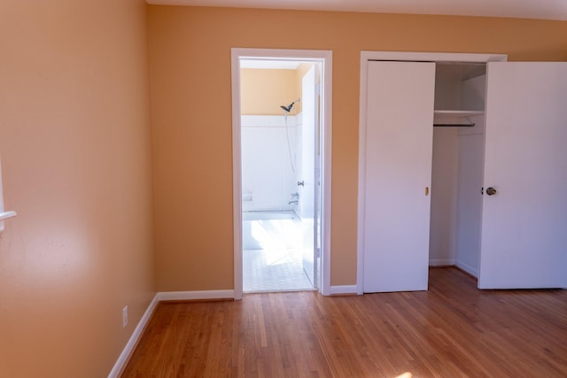 unfurnished bedroom featuring a closet, connected bathroom, baseboards, and wood finished floors