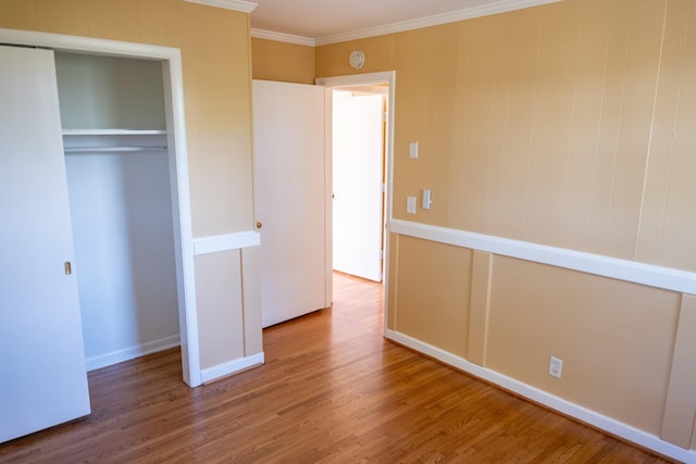 unfurnished bedroom featuring a closet, crown molding, baseboards, and wood finished floors